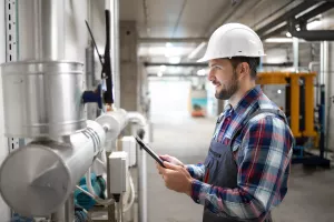 Portrait of an industrial engineer worker in protective uniform and hardhat checking valves and gas installations in factory boiler room.