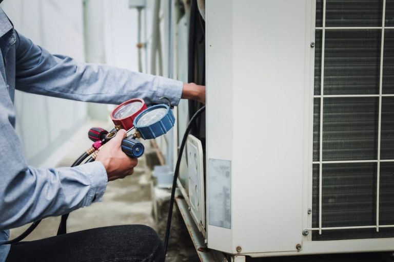 Mechanic  air conditioner technician is using a manifold gauge to check the refrigerant in the system to inspect and repair the outdoor air compressor.
