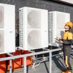 Professional workman in protective clothing adjusting the outdoor unit of the air conditioner or heat pump with digital tablet