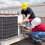 Two workers on the roof of a building working on the air conditioning unit.