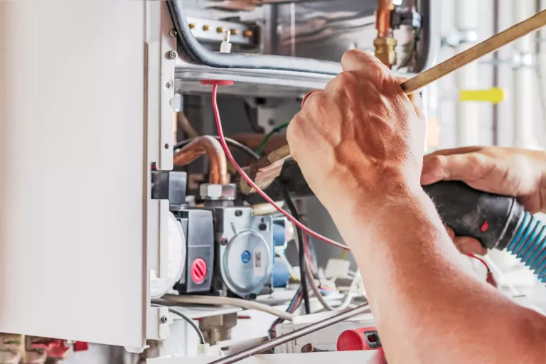 The master sets up a gas boiler, which weighs on the wall. The front dashboard is open. Using a brush and an industrial vacuum cleaner, cleaning from dirt and dirt