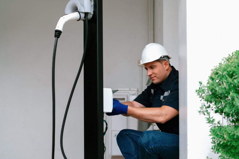 Qualified technician install home EV charging station, providing maintenance service for electric vehicle's battery charging platform at home. EV car technology for residential utilization. Synchronos