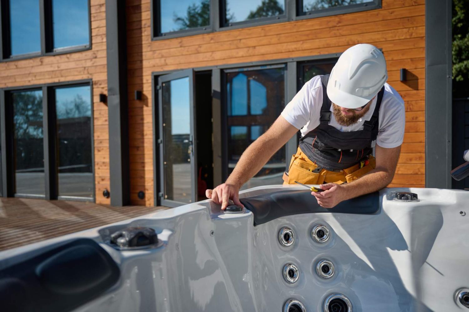Plumber installing hot tub. Spa technician performing hot tub. Bathtub plumbing. Plumber fixing spa zone. Professional in uniform inspects and prepares a hot tub located on a stylish outdoor patio.