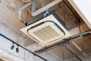Cassette type air conditioner installed on industrial loft ceiling with exposed pipes, HVAC system with ceiling mounted indoor unit of air conditioning system in modern commercial building
