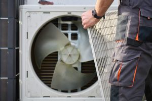 Technician removing front cover grille from outdoor heat pump unit during residential HVAC service. Concept of heat pump maintenance, repair and home heating and cooling