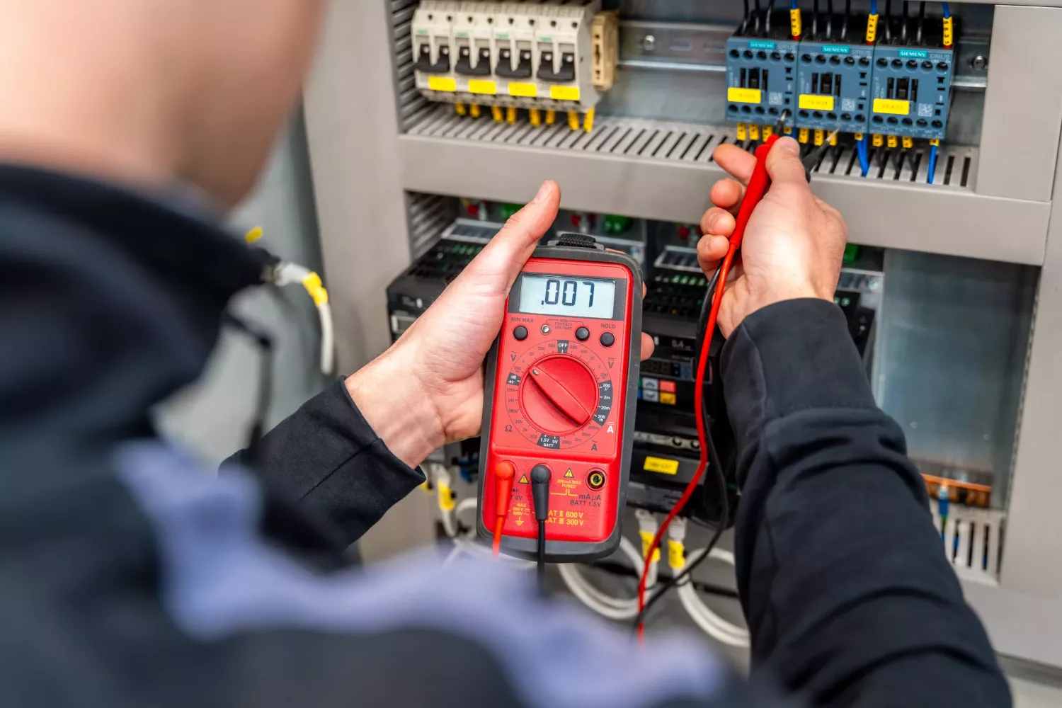 Worker measuring and repairing an electrical system panel in a factory