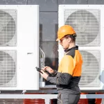 Professional workman in protective clothing adjusting the outdoor unit of the air conditioner or heat pump with digital tablet