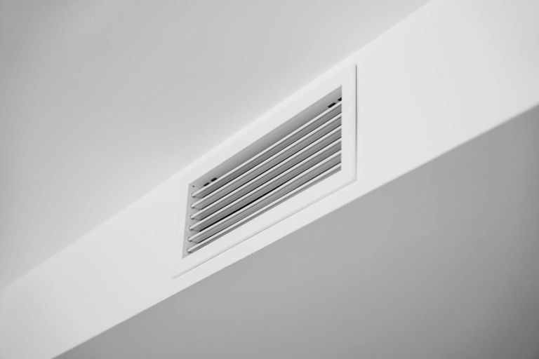 Close-up of a white ceiling ventilation grille in a modern residential interior, showcasing HVAC airflow design, minimal architecture, clean surfaces and contemporary home style.