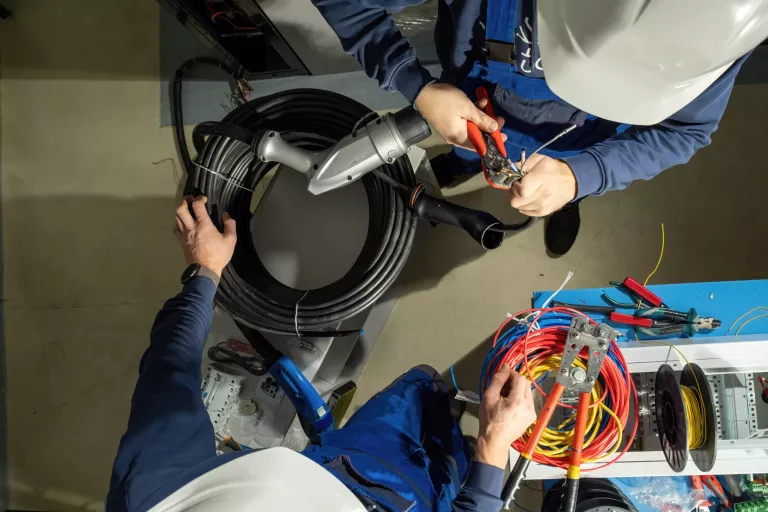 Technician works with cables for plug to charge EV. Electricians use pliers and install cables in plug for working at electric charging station