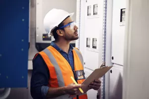Man, engineering and clipboard in control room, box inspection and machine maintenance. Male electrician, system and electrical substation for power, industrial generator and technician checklist.