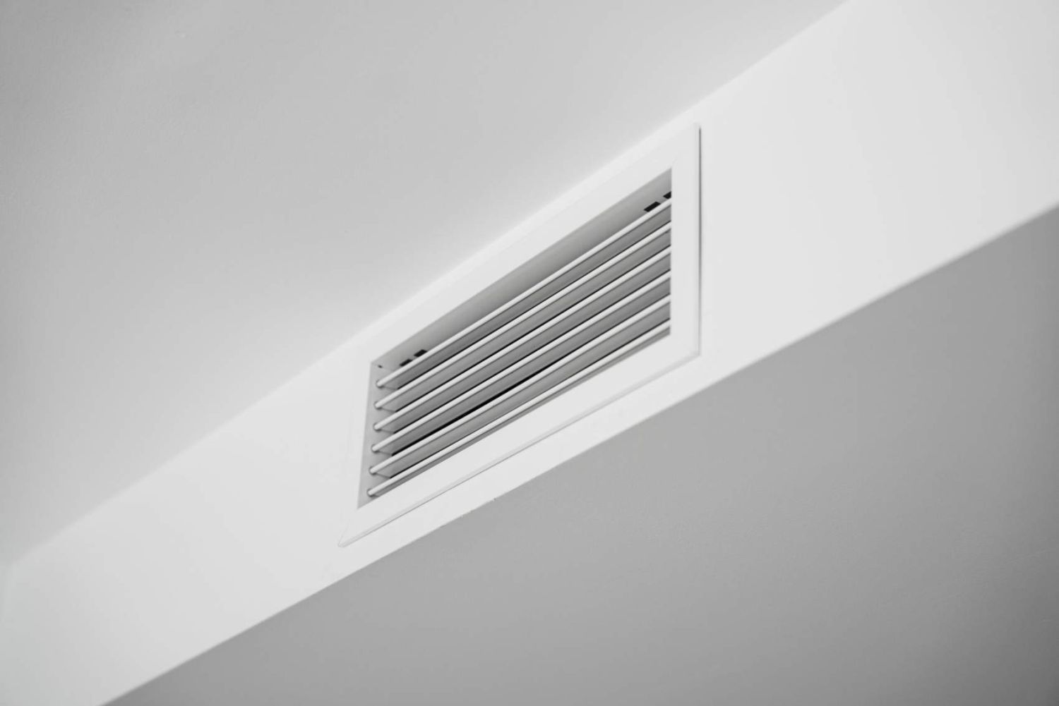 Close-up of a white ceiling ventilation grille in a modern residential interior, showcasing HVAC airflow design, minimal architecture, clean surfaces and contemporary home style.
