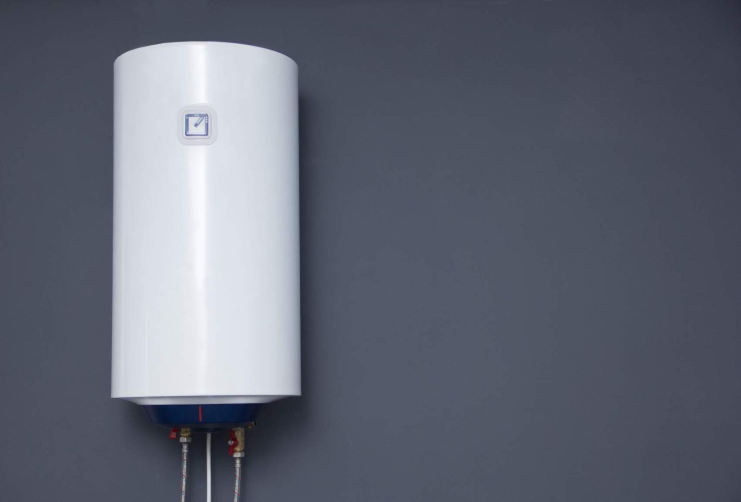 Modern electric boiler on a gray plain wall. White water heater. Space for text.