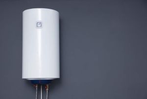 Modern electric boiler on a gray plain wall. White water heater. Space for text.