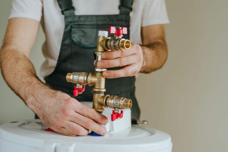 Installation of plumbing fittings on water heater by master. Close-up of male hands.