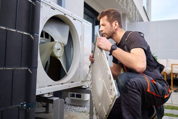 Technician removing front cover and inspecting fan inside outdoor heat pump unit. Concept of HVAC maintenance, repair service and energy efficient home heating and cooling