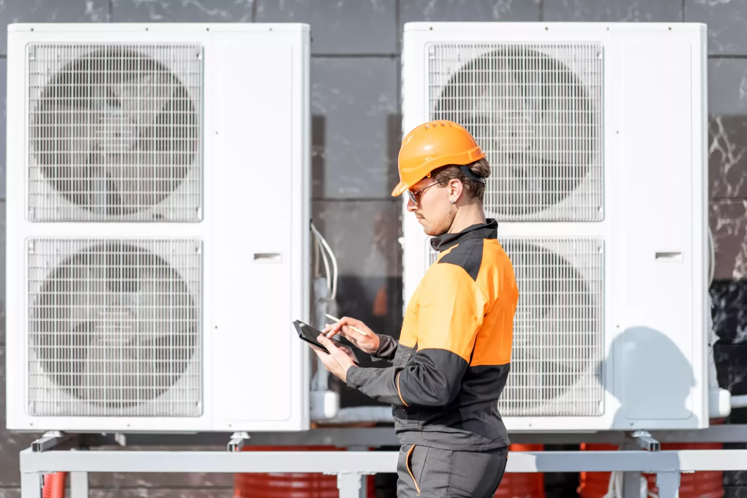 Professional workman in protective clothing adjusting the outdoor unit of the air conditioner or heat pump with digital tablet