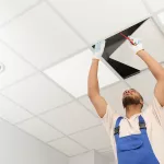 Electrician with screwdriver repairing ceiling light indoors, low angle view. Space for text